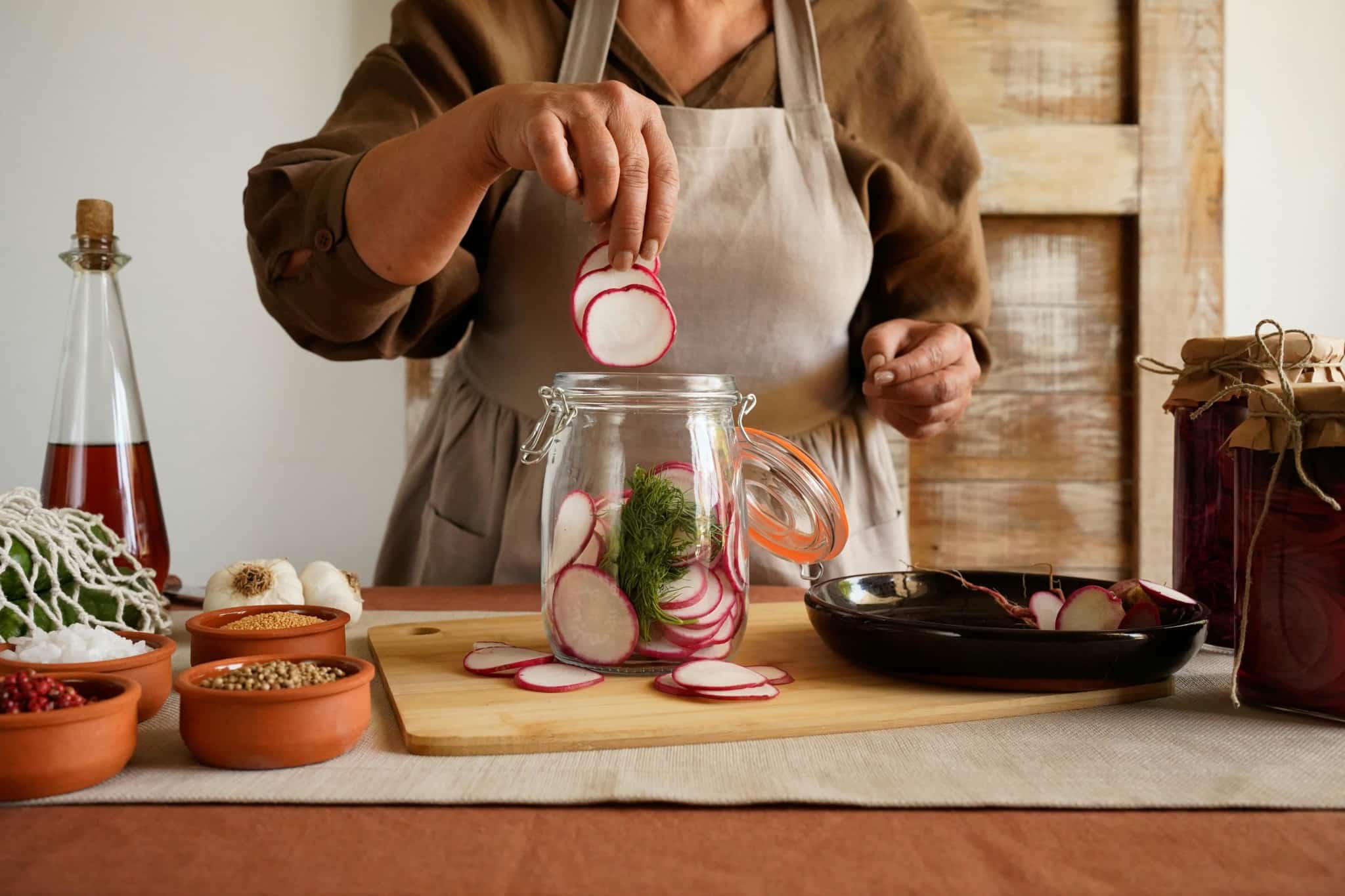 Une cheffe met des tranches de radis dans un bocal de pickles