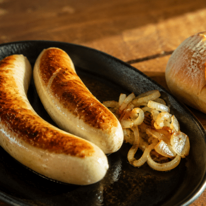 Une poêle avec deux saucisses de St Gall, des oignons blanc et une miche de pain.