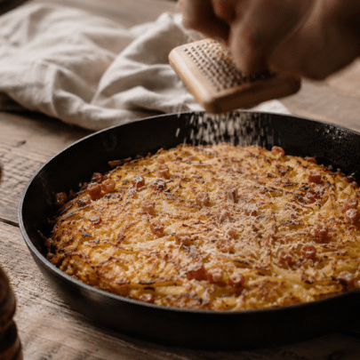 Une poêle en fonte avec le rösti bernois et quelqu'un qui râpe la muscade.